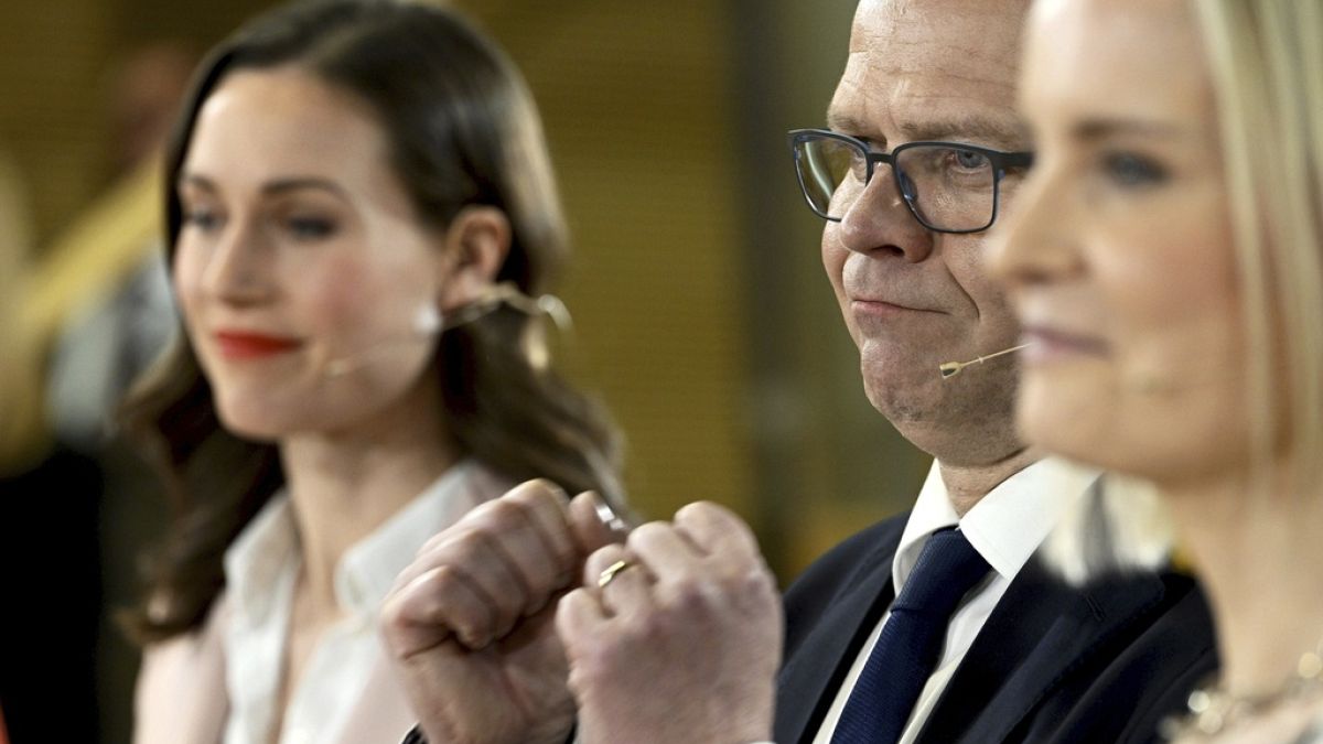 Chair of SDP Sanna Marin, left, and chair of The Finns party Riikka Purra, right, look on as National Coalition Party chair Petteri Orpo cheers at the parliamentary election.
