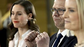 Chair of SDP Sanna Marin, left, and chair of The Finns party Riikka Purra, right, look on as National Coalition Party chair Petteri Orpo cheers at the parliamentary election.