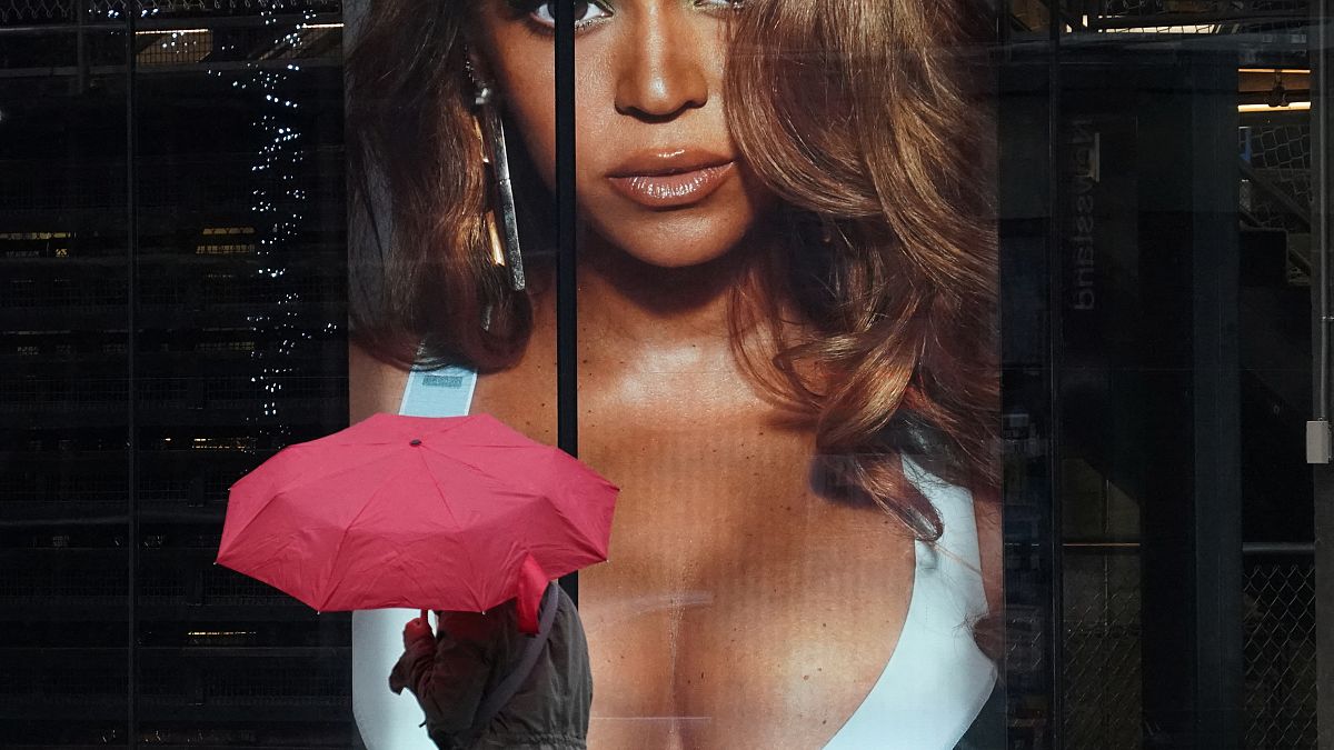 A woman holding an umbrella walks past an Adidas store that's advertising Beyonce's Ivy Park line in the window.
