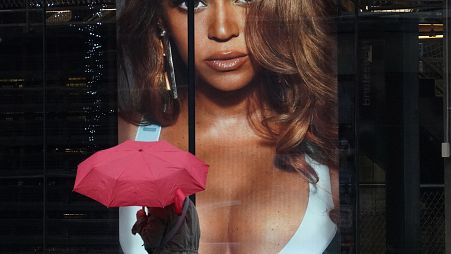 A woman holding an umbrella walks past an Adidas store that's advertising Beyonce's Ivy Park line in the window.