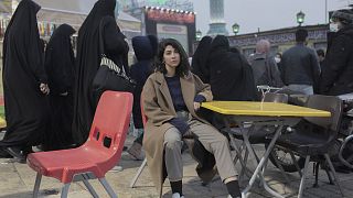 Une femme iranienne est assise sur une chaise devant une place animée de Téhéran, défiant la loi obligatoire sur le hijab
