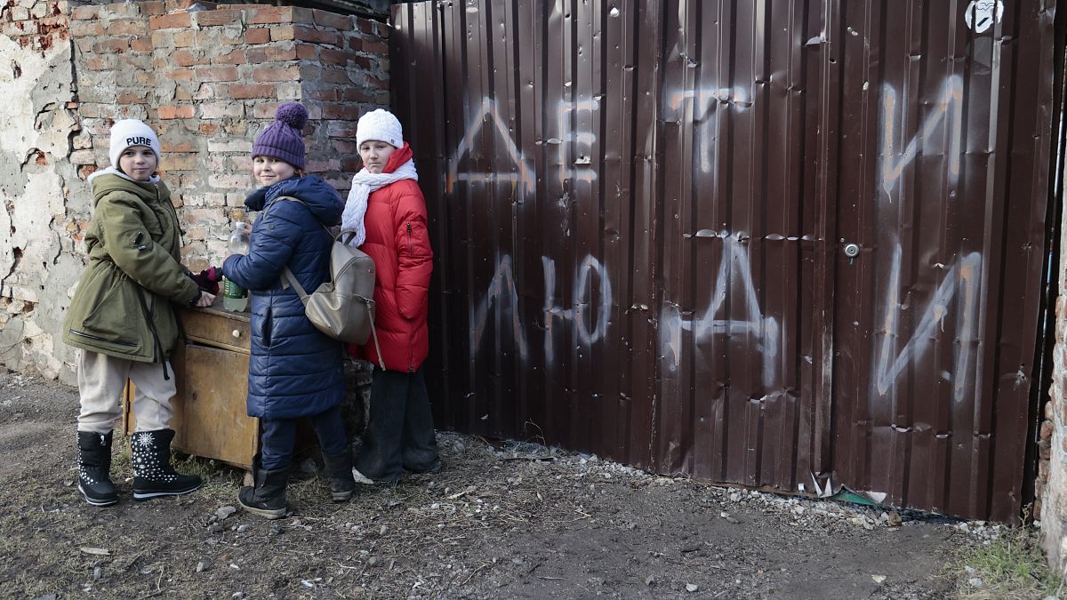 Children stand near the fence of a damaged house with the words "Children and people", Mariupol, Saturday, Feb. 25, 2023