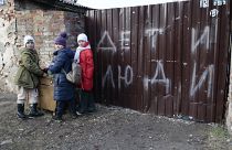 Children stand near the fence of a damaged house with the words "Children and people", Mariupol, Saturday, Feb. 25, 2023