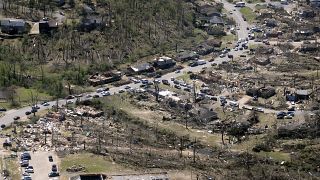 Cars line up along the road as cleanup continues from Friday's tornado damage,