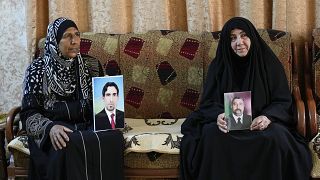 نضال علي [يمين] ونوال سويدان [يسار]، والدتان شيعية وسنيّة، تحملان صورة ابنيهما المفقودين