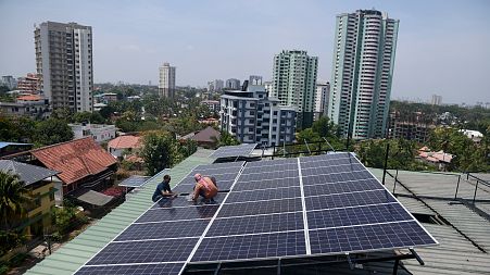 Workers install solar panels on the roof of a residential apartment in Kochi, southern Kerala state, India.