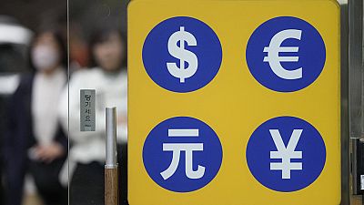 People walk near a sign of foreign currency outside a money exchange office at a shopping district in Seoul, South Korea, Tuesday, April 11, 2023. 