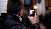 Image shows a man using the Be My Eyes app, which connects low-vision users to sighted volunteers via video call to act as their eyes.