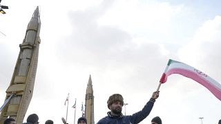 رجل يلوح بالعلم الإيراني بجانب صواريخ محلية الصنع