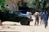 Civis em fuga junto de um veículo militar na capital do Sudão, Cartum