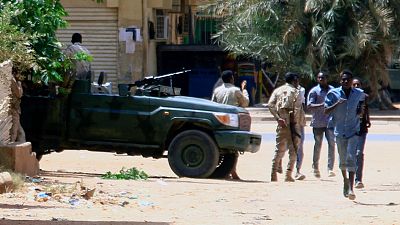 Civis em fuga junto de um veículo militar na capital do Sudão, Cartum