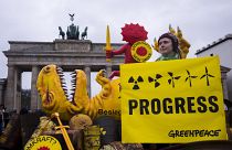 A Greenpeace activist poses with a poster in front of a mock-up dinosaur in front of the Brandenburg Gate during a rally marking the nuclear shutdown in Germany, 15 April 2023