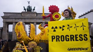 A Greenpeace activist poses with a poster in front of a mock-up dinosaur in front of the Brandenburg Gate during a rally marking the nuclear shutdown in Germany, 15 April 2023