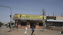 People walk past shuttered shops in Khartoum, Sudan, Tuesday, April 18, 2023. 