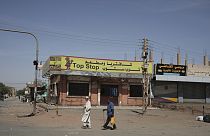 People walk past shuttered shops in Khartoum, Sudan, Tuesday, April 18, 2023.