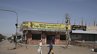 People walk past shuttered shops in Khartoum, Sudan, Tuesday, April 18, 2023. 
