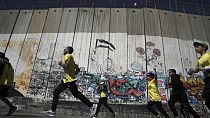  عداؤون يجتازون الجدار  الإسرائيلي الفاصل الذي  بنته إسرائيل أثناء مشاركتهم في ماراثون فلسطين في مدينة بيت لحم بالضفة الغربية، 10 مارس ، 2023