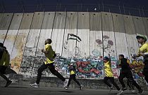  عداؤون يجتازون الجدار  الإسرائيلي الفاصل الذي  بنته إسرائيل أثناء مشاركتهم في ماراثون فلسطين في مدينة بيت لحم بالضفة الغربية، 10 مارس ، 2023