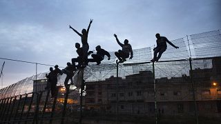 Migrantes subsarianos trepam por cima de uma vedação metálica que divide Marrocos e o enclave espanhol de Melilla, 29 de março de 2014