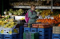 Женщина покупает в уличной лавке фрукты и овощи