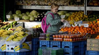 Женщина покупает в уличной лавке фрукты и овощи