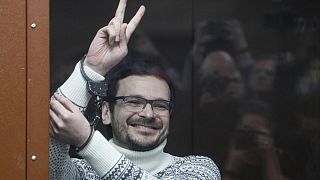 Russian opposition activist Ilya Yashin gestures, smiling, as he stands in a defendant's cubicle prior to his original sentencing in December 2022.