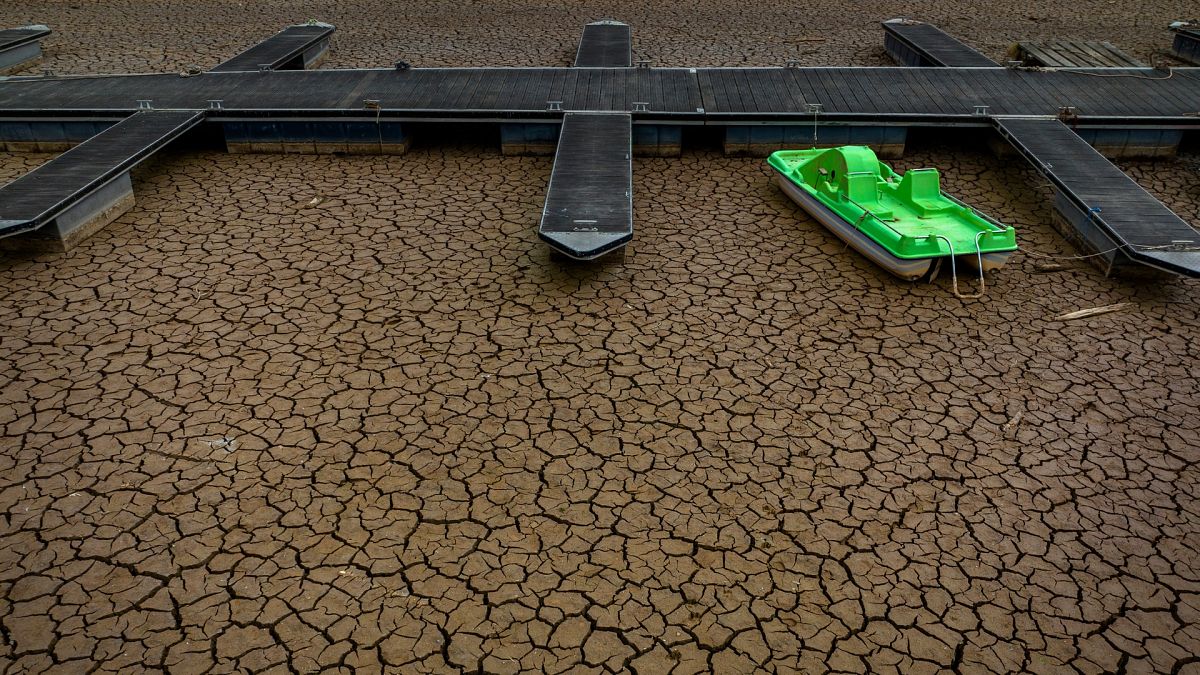 A green pedal boat is tied to a dock in a dried part of the Sau reservoir.