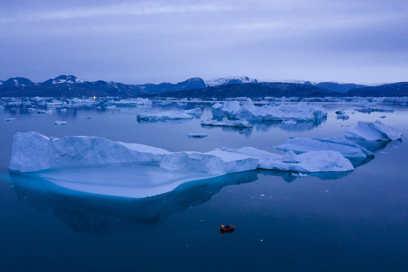 Bir tekne geceleri Grönland'ın doğusundaki Kulusuk kasabası yakınlarındaki büyük buzdağlarının yanında seyrediyor.