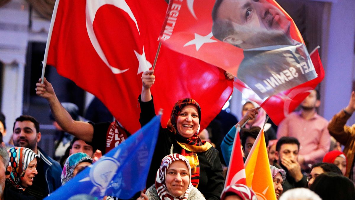 FILE - In this March 6, 2017 file photo women wave a Turkish flag and a flag showing President Erdogan, near Frankfurt