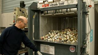 A worker prepares to press the button of a machine to crush empty Miller High Life beer cans at the Westlandia plant in Ypres, Belgium.