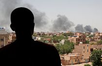 Um homem observa a coluna de fumo sobre a capital do Sudão