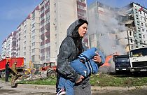 A woman walks past damaged residential buildings as she carries a child in Uman, around 215km southern Kyiv, on April 28, 2023