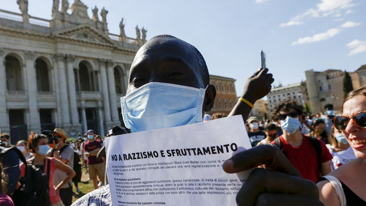 A man holds a leaflet with the headline reading 'No to racism and exploitation' during a rally for the rights of the most vulnerable workers in Rome in 2020.