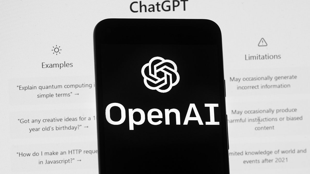 The OpenAI logo is seen on a mobile phone in front of a computer screen which displays the ChatGPT home Screen, on March 17, 2023, in Boston.