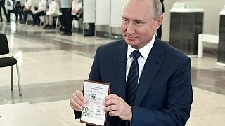 ولادیمیر پوتین گذرنامه خود را در انتخابات روسیه در پای صندوق رای نشان می‌دهد