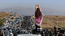 An unveiled woman stands on the roof of a vehicle as thousands march towards Mahsa Amini's hometown in October 2022.