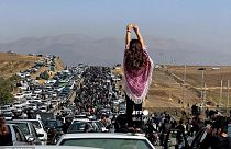 An unveiled woman stands on the roof of a vehicle as thousands march towards Mahsa Amini's hometown in October 2022.