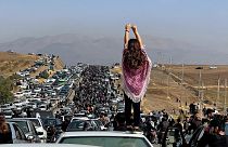Une femme non voilée se tient sur le toit d'un véhicule alors que des milliers de personnes se dirigent vers la ville natale de Mahsa Amini. Octobre 2022