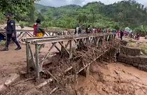 People walk across a bridge strewn with flood debris in western Rwanda on Wednesday, May 3, 2023. 