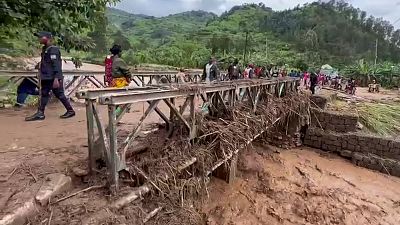 People walk across a bridge strewn with flood debris in western Rwanda on Wednesday, May 3, 2023. 