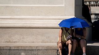 As pessoas usam um guarda-chuva para se abrigarem do sol perto da Pirâmide du Louvre, Paris, Junho de 2019.