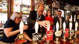 Vilmos herceg sört csapol egy londoni pubban, mögötte piros ruhában Katalin hercegnő 2023.05.04-én.