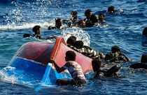 Мигранты рядом с перевернутой лодкой во время спасательной операции на юге итальянского о-ва Лампедуза в Средиземном море (11 августа 2022 г.)