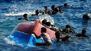 Мигранты рядом с перевернутой лодкой во время спасательной операции на юге итальянского о-ва Лампедуза в Средиземном море (11 августа 2022 г.)