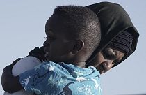 Egy kimenekített szudáni nő viszi a fiát, miközben elhagyják az USNS Brunswick nevű hajót a szaúd-arábiai Dzsidda kikötőjében 2023. május 4-én,