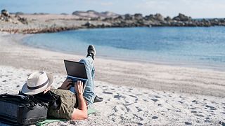A man using his laptop on the beech.