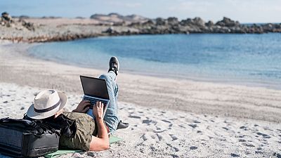 A man using his laptop on the beech. 