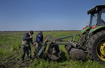 Két mezőgazdasági dolgozó sarat távolít el egy traktorról