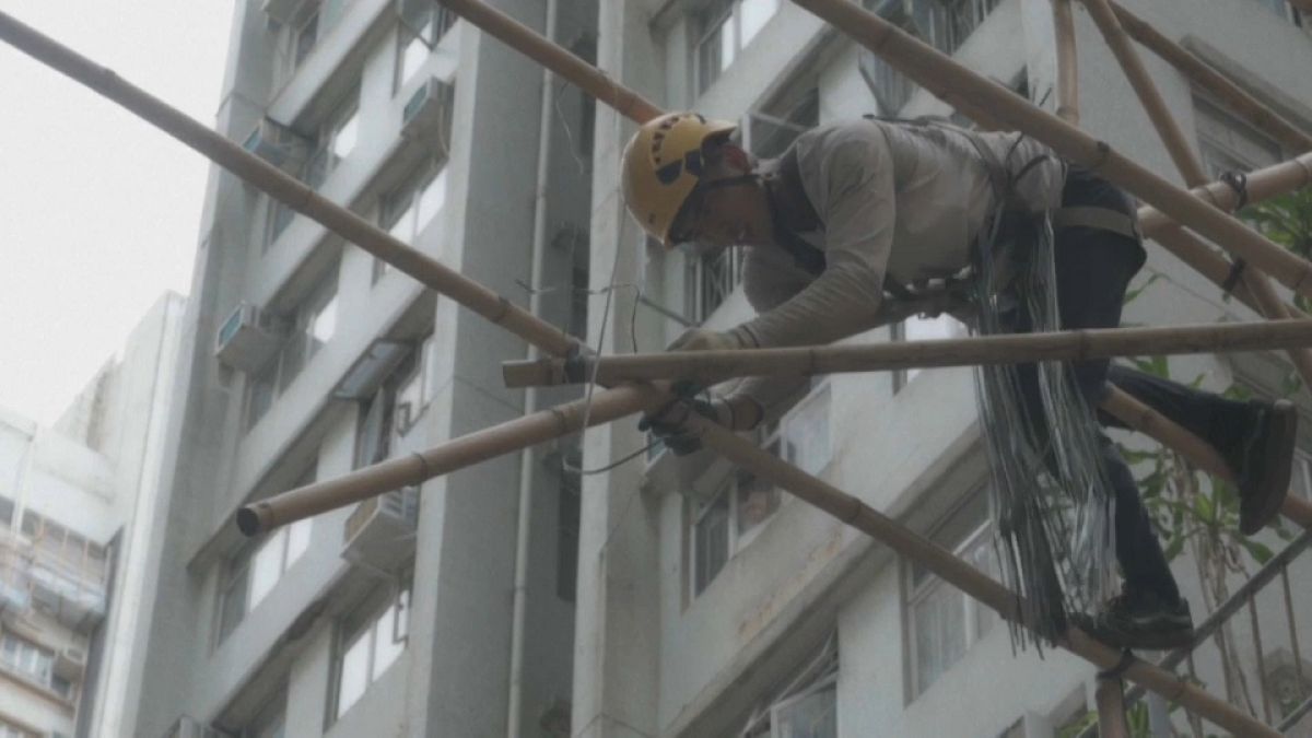 A worker builds bamboo scaffolding for an overhanging shop sign
