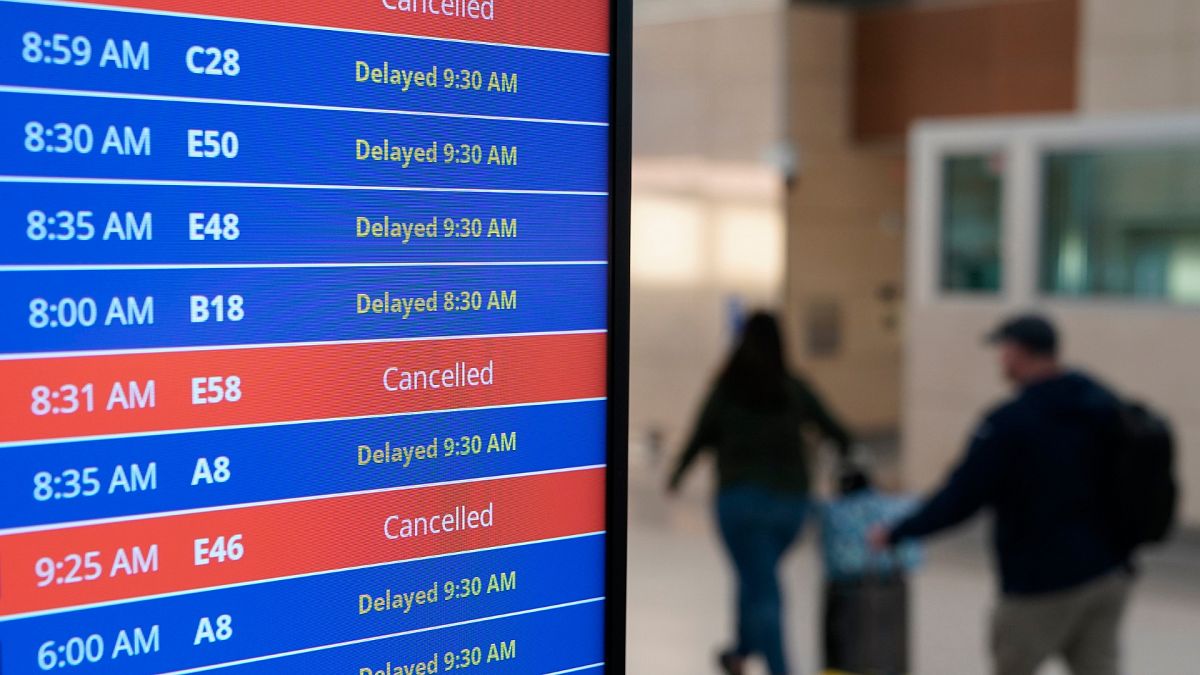 Travellers walk as a video board shows flight delays and cancellations at Ronald Reagan Washington National Airport. 